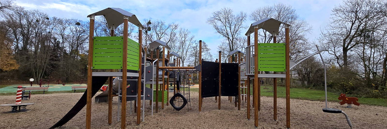 A large wooden playground unit, with green panels and lots of play experiences.
